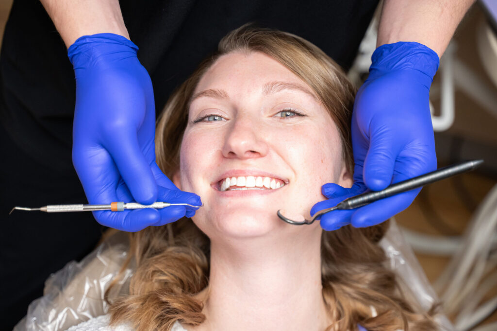 Smiling female dental patient with dentist’s gloved hands beside face