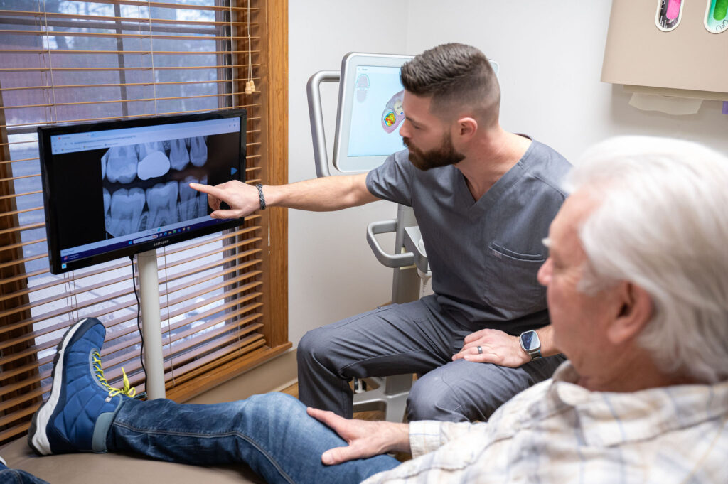 Dr. Jonathan Wells pointing at a dental X-ray on a monitor while a patient sits in the dental chair.