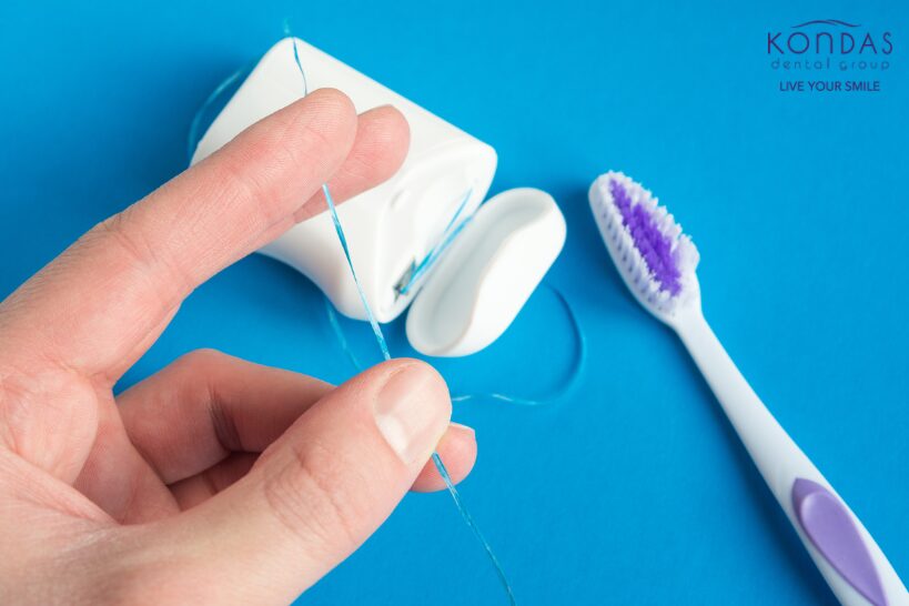 Hand holding dental floss beside an open floss container and toothbrush on a blue background, promoting daily flossing for healthy gums.